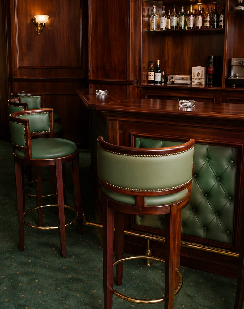 Mahogany bar with a buttoned green leather front and matching swivel bar stools